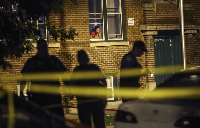 A woman watches from her window as police look for evidence after 20-year-old Carlos Barron was shot and killed in Chicago. The city is still very racially segregated and has high rates of violence.