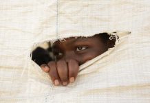 A Zimbabwean secondary school student peeps through a hole in a sack that forms the wall of a makeshift classroom.