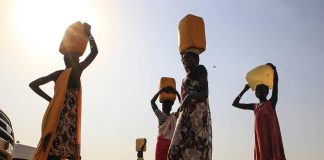 Displaced people carry water containers on their heads at Tomping camp