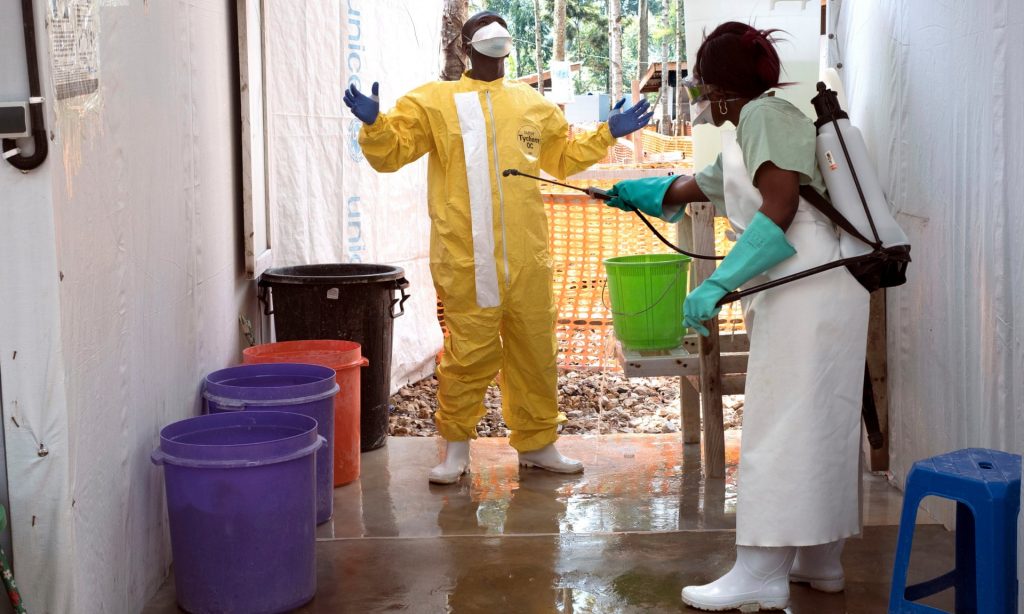 A female healthworker sprays down a male healthworker in an Ebola protective suit.