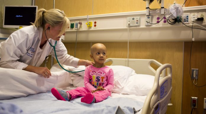 A doctor bends down to check young cancer patient's heartbeat.